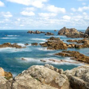 Das Wandbild Bretonische Küste zeigt die markante Felsenlandschaft der Bretagne mit weich fließendem Wasser in einer Langzeitbelichtung unter blauem Himmel