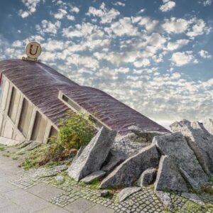 Das Composing Downstairs Underground zeigt einen surrealen U-Bahn-Aufgang, der organisch aus einem Felsen unter einem weiten Wolkenhimmel ragt.