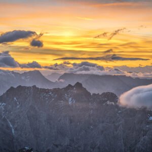 Fotokunst Der Tag beginnt Zugspitze: Aufnahme eines dunklen Felsmassivs unter gelb leuchtenden Wolken bei Sonnenaufgang.
