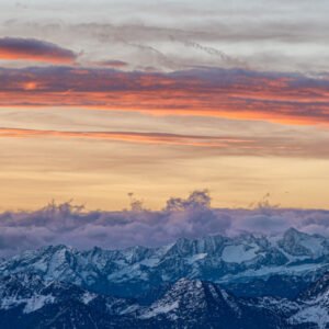 Fotokunst Gipfelwolken Zugspitze: Schneebedeckte Berggipfel unter einem Himmel mit orange leuchtenden Wolkenbändern.