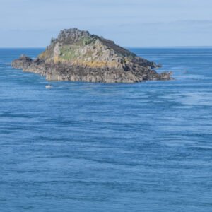 Das Wandbild Eine Insel im Meer zeigt eine schroffe Felseninsel im tiefblauen Ozean mit einem fernen Leuchtturm am Horizont