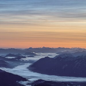 Fotokunst Nebelmeer Zugspitze: Weitläufige Bergketten in Blau- und Violetttönen mit nebelgefüllten Tälern unter einem pastellfarbenen Himmel.