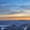 Fotokunst Perfekter Morgen Zugspitze: Weites Panorama mit Nebel in den Tälern und gelb-blauem Himmel bei Sonnenaufgang.