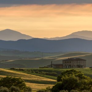 Das Wandbild Toskanischer Abend zeigt ein einsames Landhaus in den sanften Hügeln der Toskana vor einer imposanten Bergkulisse im warmen Abendlicht