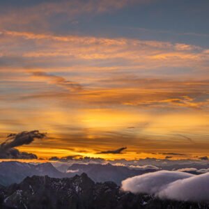 Fotokunst Von der Zugspitze: Dramatischer Sonnenaufgang mit intensiv orange-gelb leuchtenden Wolken über dunklen Bergsilhouetten.