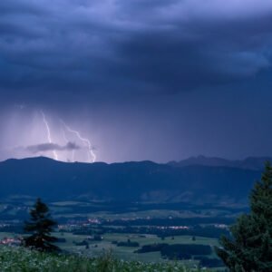 Das Wandbild Alpengewitter zeigt mehrere helle Blitze, die während der blauen Stunde über einer dunklen Alpenkette in einen dramatischen, bewölkten Nachthimmel zucken.