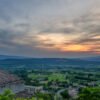 Das Panorama-Wandbild Blick ins Land zeigt ein historisches Ziegeldach mit schmiedeeisernem Glockenturm im Vordergrund und eine weite, sonnenbedeckte Tallandschaft der Provence.