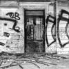 Schwarz-weiß Fotografie Czech Graffity zeigt eine verfallene Fassade mit ausdrucksstarken Graffiti und einer alten Holztür.