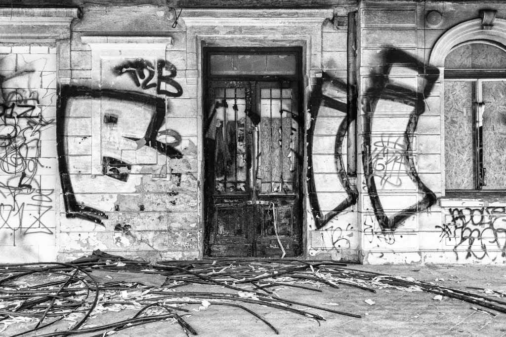 Schwarz-weiß Fotografie Czech Graffity zeigt eine verfallene Fassade mit ausdrucksstarken Graffiti und einer alten Holztür.