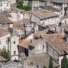 Das Wandbild Dächer einer Altstadt zeigt eine dichte Ansammlung historischer Ziegeldächer und Steinfassaden in Südfrankreich aus einer erhöhten Perspektive.