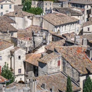 Das Wandbild Dächer einer Altstadt zeigt eine dichte Ansammlung historischer Ziegeldächer und Steinfassaden in Südfrankreich aus einer erhöhten Perspektive.