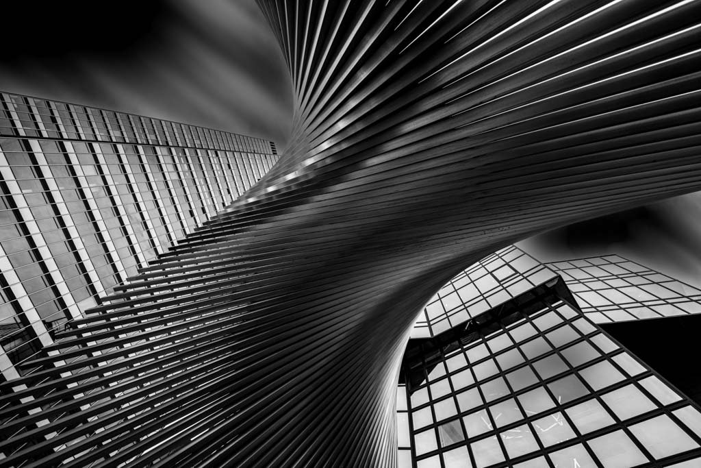 Die schwarz-weiß Fotografie From Underneath zeigt eine dynamisch geschwungene Treppenstruktur vor einer modernen Glasfassade in extremer Froschperspektive.