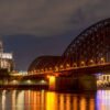 Das Panorama-Wandbild Köln bei Nacht zeigt den beleuchteten Kölner Dom und die Hohenzollernbrücke mit Spiegelungen im Rhein.