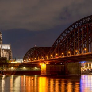 Das Panorama-Wandbild Köln bei Nacht zeigt den beleuchteten Kölner Dom und die Hohenzollernbrücke mit Spiegelungen im Rhein.