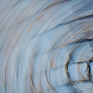 Das Wandbild Kopfsteinstrudel zeigt eine abstrakte ICM-Aufnahme von Kopfsteinpflaster, das durch eine kreisförmige Kamerabewegung in einen dynamischen Strudel aus Blau- und Grautönen verwandelt wurde.