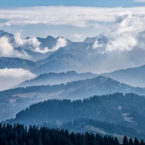 Das Wandbild Mountain Mist zeigt eine tief gestaffelte Berglandschaft im Allgäu, bei der dunkle Nadelwälder im Vordergrund in blau-graue Bergsilhouetten übergehen, die von weißen Wolken und Nebel umspielt werden.