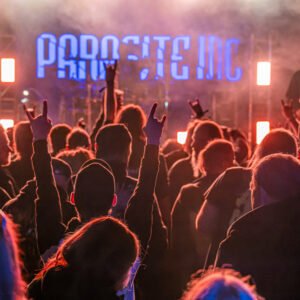 Das Wandbild Parasite Inc zeigt die jubelnde Menschenmenge mit „Pommesgabel“-Gesten vor der beleuchteten Bühne der Metal-Band im 3:2 Format.