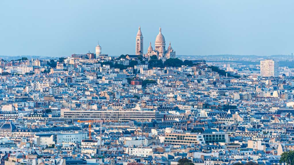 Das Panorama-Wandbild Sacre Coeur zeigt die weiße Basilika auf dem Montmartre über dem dichten Häusermeer von Paris bei hellem Tageslicht.