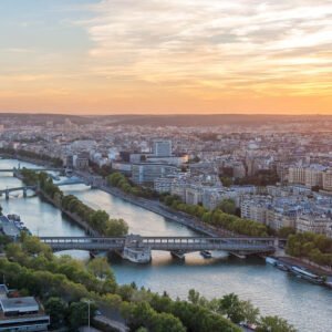 Das Panorama-Wandbild Paris am Abend zeigt den weiten Blick über die Seine und die Stadtarchitektur im goldenen Licht des Sonnenuntergangs.