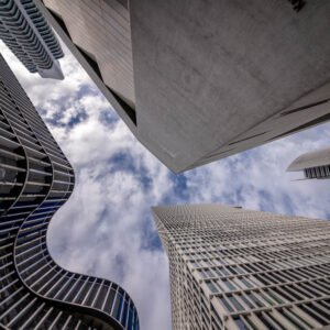 Das Wandbild Schau nach oben in Frankfurt zeigt eine beeindruckende Untersicht moderner Wolkenkratzer vor einem leicht bewölkten Himmel im 3:2 Format.