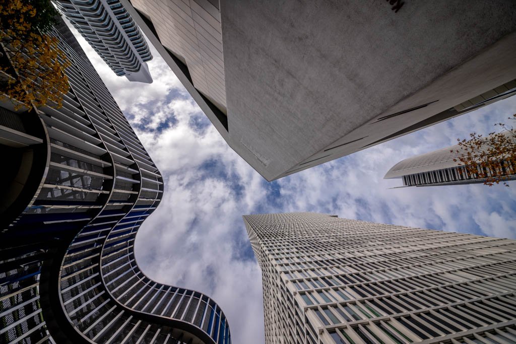 Das Wandbild Schau nach oben in Frankfurt zeigt eine beeindruckende Untersicht moderner Wolkenkratzer vor einem leicht bewölkten Himmel im 3:2 Format.