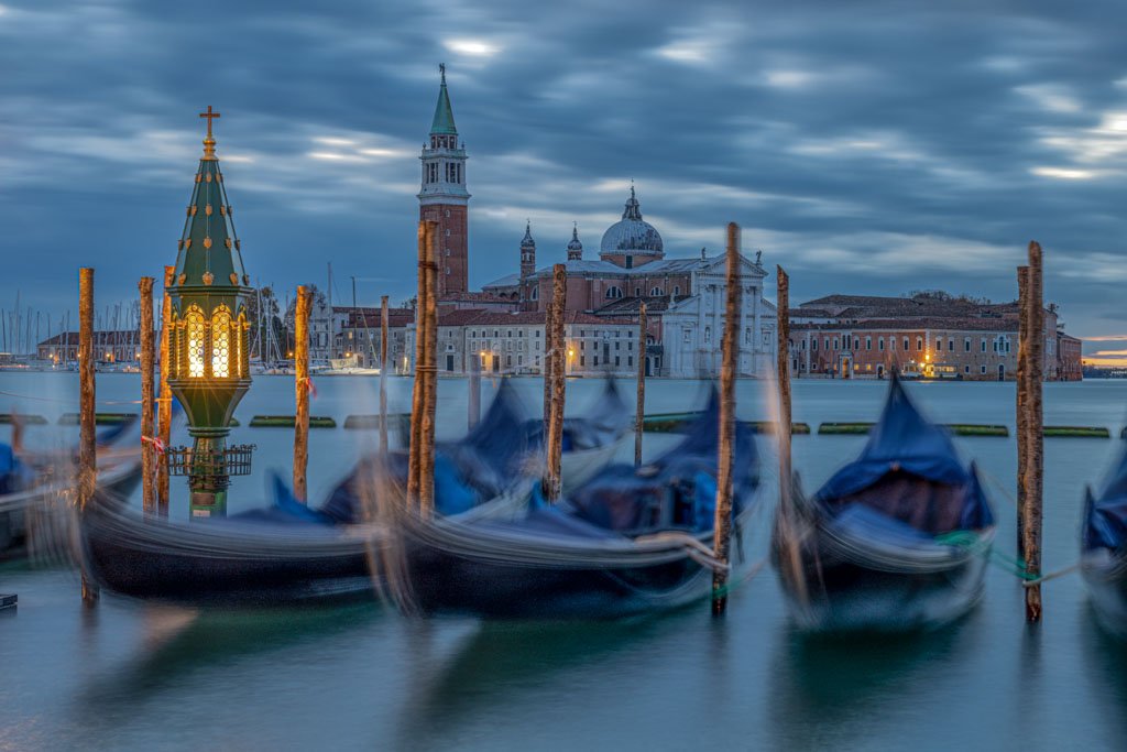 Das Wandbild Schlafende Gondeln zeigt blau abgedeckte Gondeln in Venedig vor der Basilika San Giorgio Maggiore in der blauen Stunde.