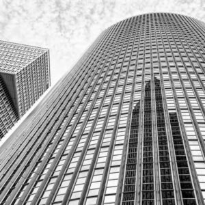 Das Wandbild Spiegelung in Schwarz-Weiß zeigt eine abstrakte Untersicht moderner Hochhausfassaden mit markanten Spiegelungen im 3:2 Format.