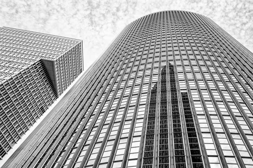 Das Wandbild Spiegelung in Schwarz-Weiß zeigt eine abstrakte Untersicht moderner Hochhausfassaden mit markanten Spiegelungen im 3:2 Format.