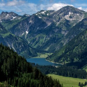 Das Wandbild Vilsalpsee zeigt den tiefblauen Bergsee in den Allgäuer Alpen, umgeben von steilen, bewaldeten Berghängen und markanten, felsigen Gipfeln unter einem leicht bewölkten Sommerhimmel.