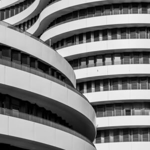 Das Wandbild Wellenbalkone zeigt eine abstrakte Schwarz-Weiß-Aufnahme geschwungener Fassadenelemente eines modernen Gebäudes im 3:2 Format.