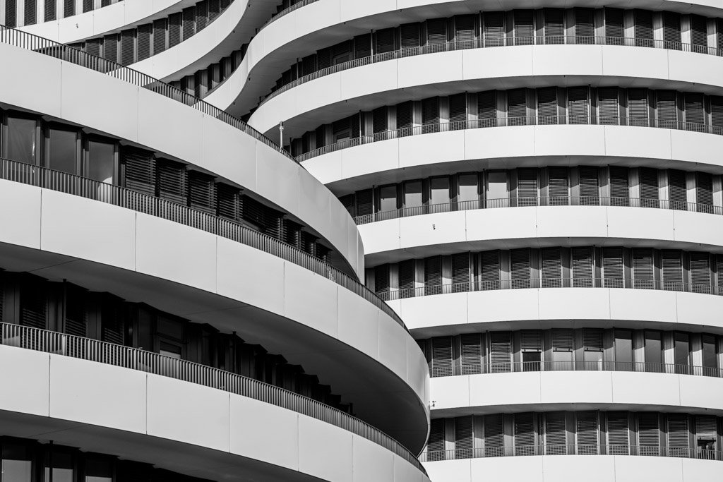 Das Wandbild Wellenbalkone zeigt eine abstrakte Schwarz-Weiß-Aufnahme geschwungener Fassadenelemente eines modernen Gebäudes im 3:2 Format.