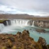 Das Wandbild Goðafoss zeigt den imposanten isländischen Wasserfall in einer weichen Langzeitbelichtung mit türkisfarbenem Wasser unter bewölktem Himmel