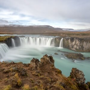 Das Wandbild Goðafoss zeigt den imposanten isländischen Wasserfall in einer weichen Langzeitbelichtung mit türkisfarbenem Wasser unter bewölktem Himmel