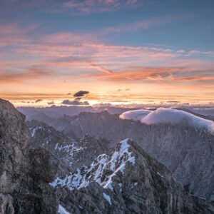 Fotokunst Zugspitzgipfel: Panoramaaufnahme mit dem markanten Gipfelkreuz links im Vordergrund vor einer weiten Alpenkulisse im Sonnenaufgang.