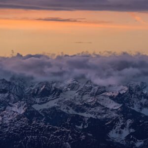 Fotokunst Zugspitzschnee Panorama: Schneebedeckte Alpengipfel unter einer dramatischen Wolkenschicht im warmen Licht der Dämmerung.