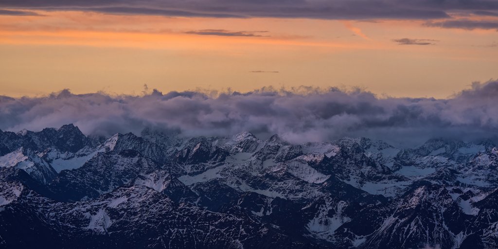 Fotokunst Zugspitzschnee Panorama: Schneebedeckte Alpengipfel unter einer dramatischen Wolkenschicht im warmen Licht der Dämmerung.