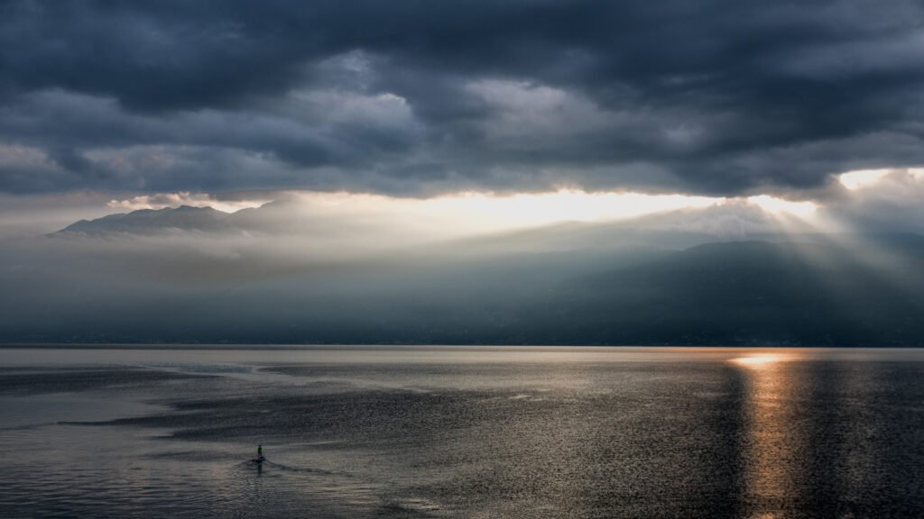 Gewitterstimmung am Gardasee mit Sonnenstrahl auf dem Wasser und SUP-Paddler – Fotografie Roland Seichter.