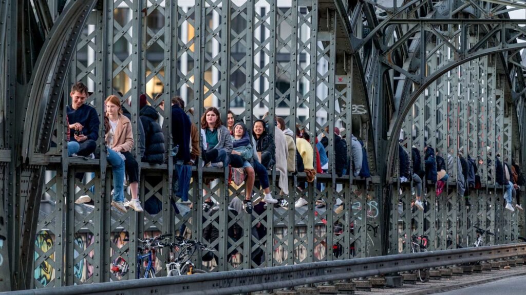 Viele junge Menschen sitzen auf den Stahlverstrebungen der Hackerbrücke in München bei Sonnenuntergang.