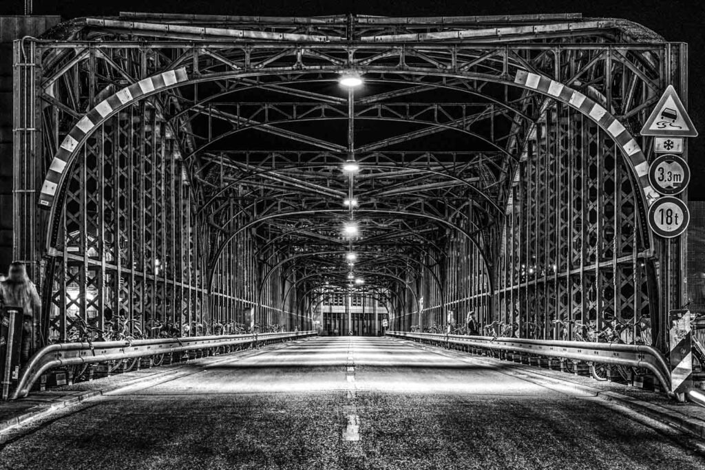 Symmetrische Nachtaufnahme der Stahlkonstruktion der Hackerbrücke in München in Schwarz-Weiß.
