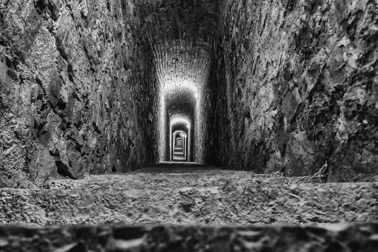 Blick durch einen tiefen, beleuchteten historischen Mauertunnel mit Steintreppen.