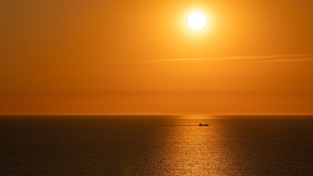 Abendliche Landschaftsfotografie am Meer: Sonnenspiegelung und Schiff-Schattenriss am Horizont.