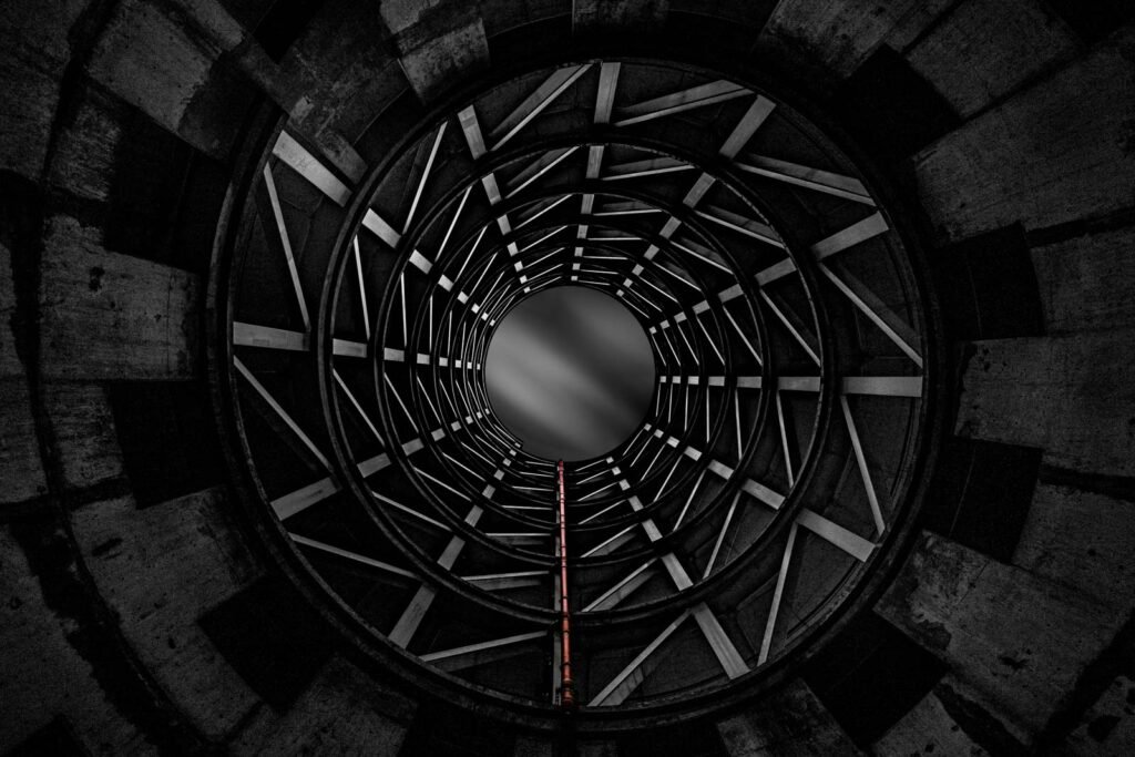 Abstrakte Schwarz-Weiß-Ansicht von unten in einen industriellen Schornstein mit kreisförmigen Stahlverstrebungen.