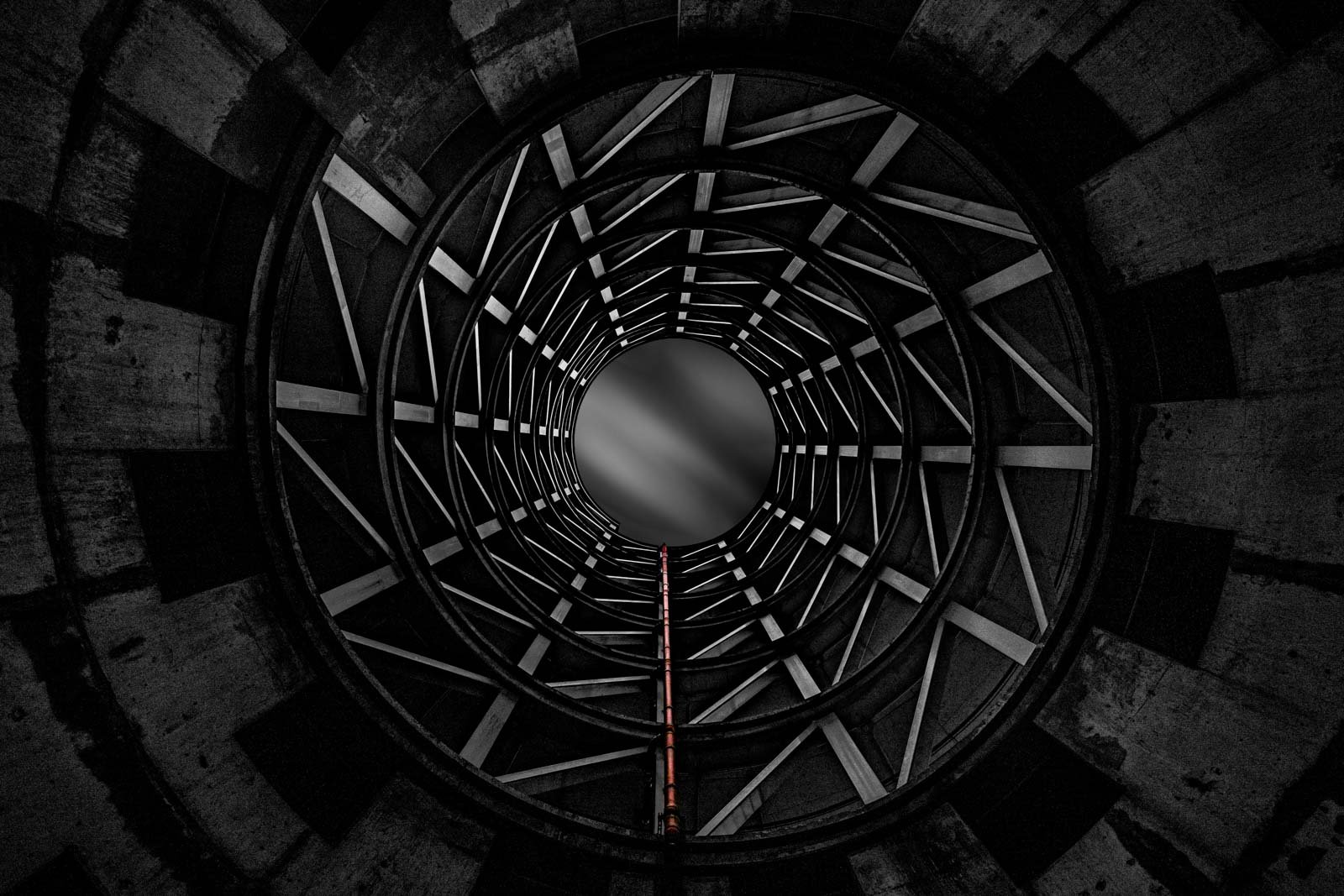 Abstrakte Schwarz-Weiß-Ansicht von unten in einen industriellen Schornstein mit kreisförmigen Stahlverstrebungen.