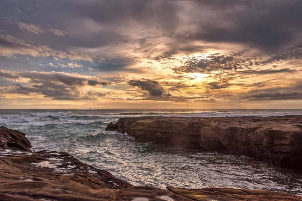 Dramatischer Sonnenuntergang über einer felsigen Küstenlinie mit brandenden Wellen.