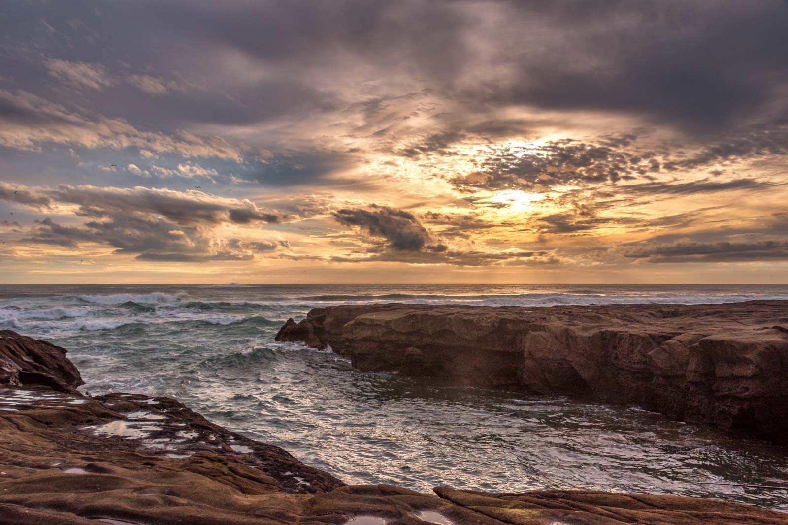 Dramatischer Sonnenuntergang über einer felsigen Küstenlinie mit brandenden Wellen.