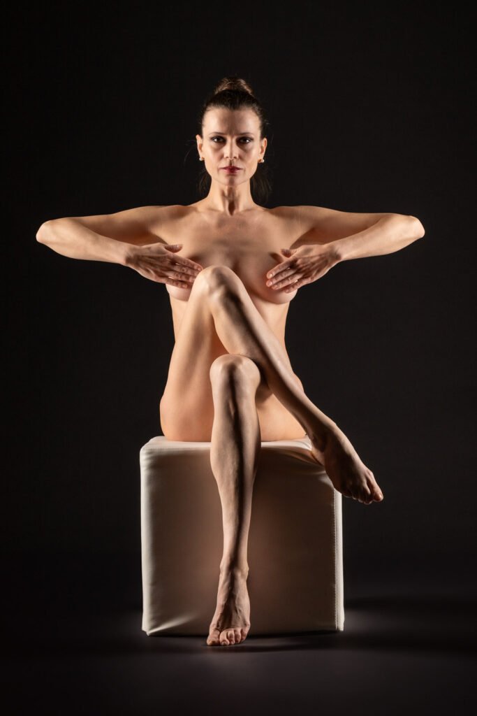 Ästhetische Aktaufnahme einer sitzenden Frau vor schwarzem Hintergrund in einer symmetrischen Pose