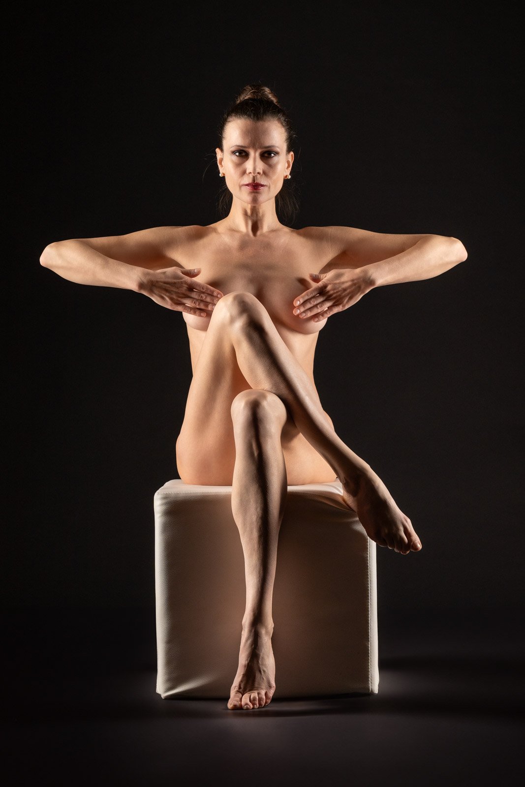 Ästhetische Aktaufnahme einer sitzenden Frau vor schwarzem Hintergrund in einer symmetrischen Pose