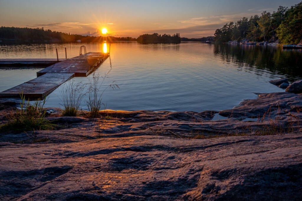 Blick in die Abendsonne über den Schärenfelsen mit Badesteg – Fotokunst von Roland Seichter.
