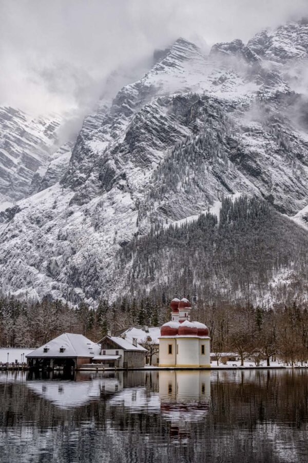 Landschaftsfotografie Königssee: St. Bartholomä Kapelle im Hochformat vor markantem Winter-Alpenmassiv.