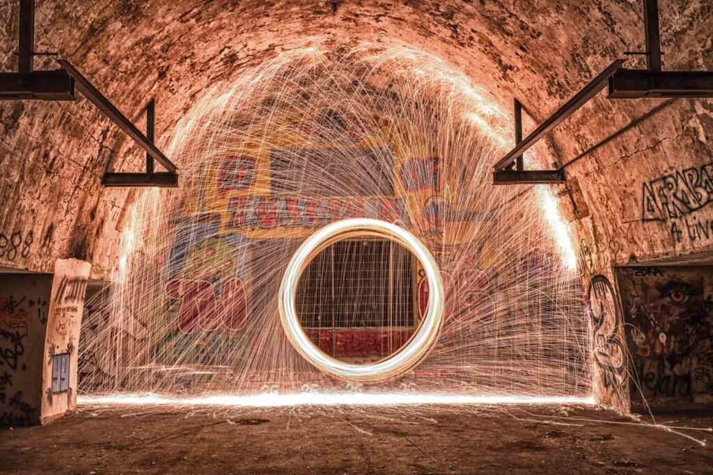Lightpainting-Fotografie in einem verlorenen Ort mit einem brennenden Stahlwolle-Ring und sprühenden Funken vor Graffiti-Wänden.